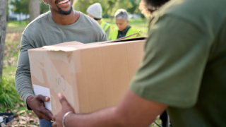 Man volunteering and giving box in park of donation, community service or social responsibility.