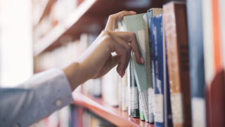 A man reaching for a book off of a library shelf